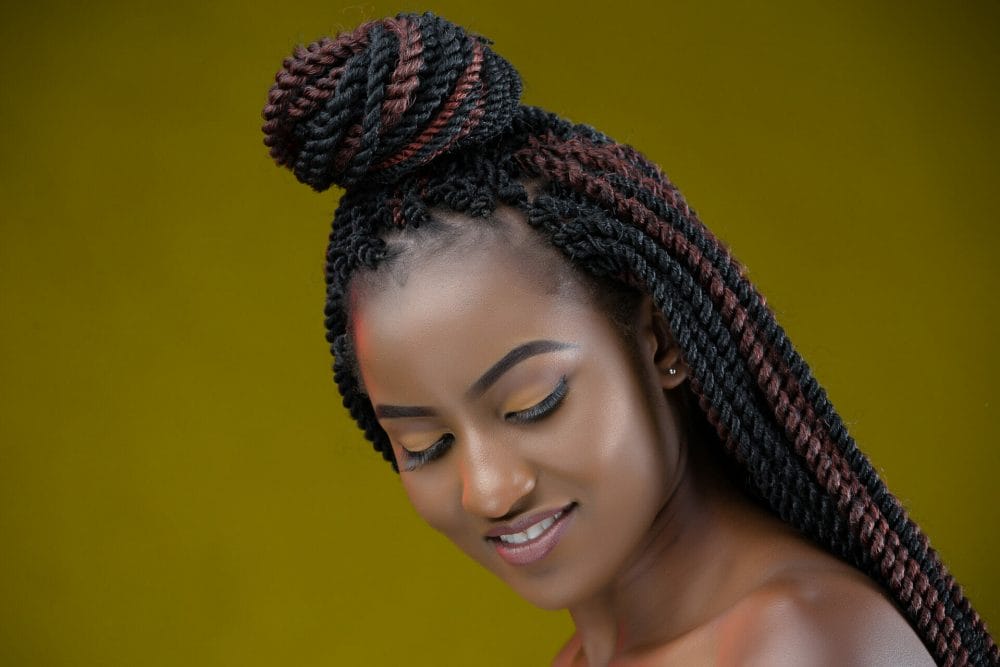 woman portrait with knotless braids looking down and smiling on a dark-yellow background