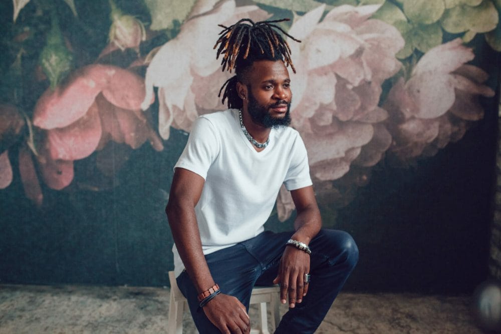 man with locs-style knotless braids with a background of a wall painted with flowers