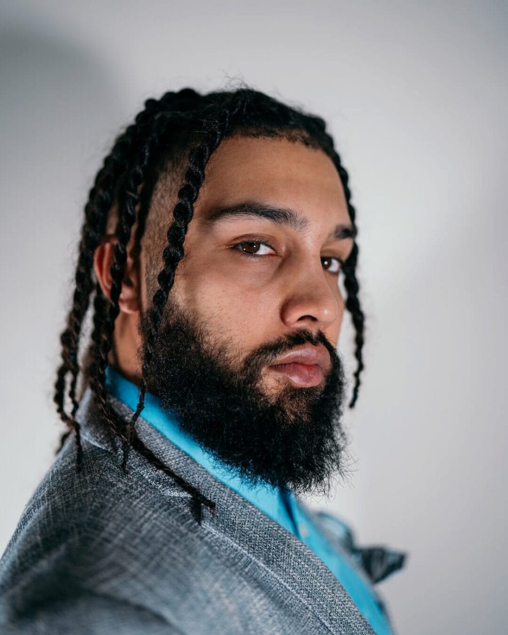 man with twists-style knotless braids and a beard, wearing a blue jacket on white background