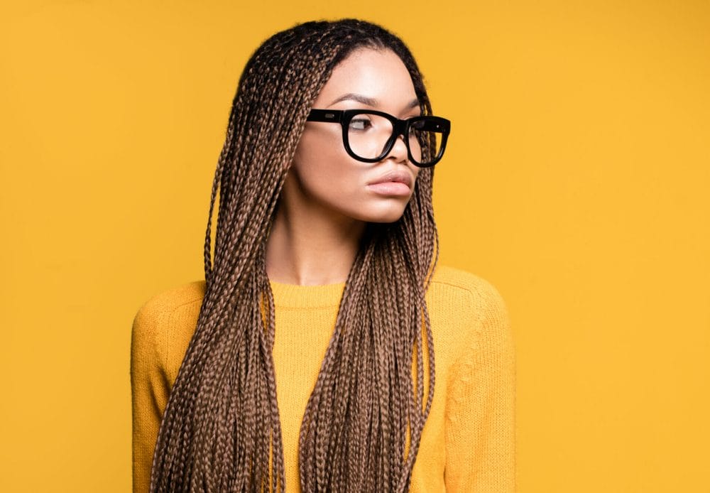 woman with knotless braids and glasses posing on a yellow background