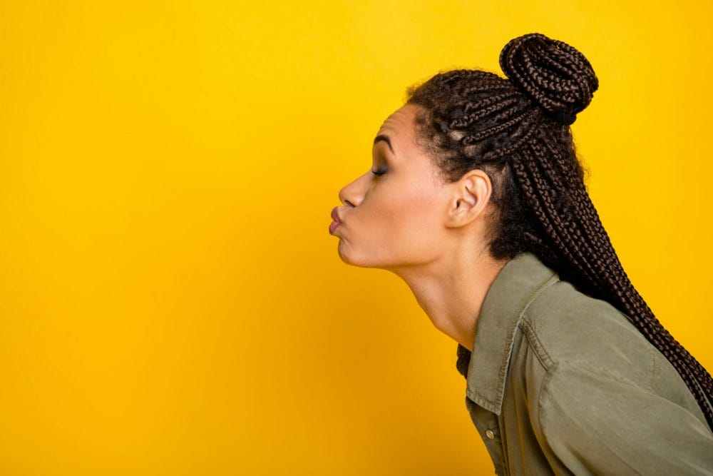 woman side profile-view with knotless braids blowing a kiss on a yellow background